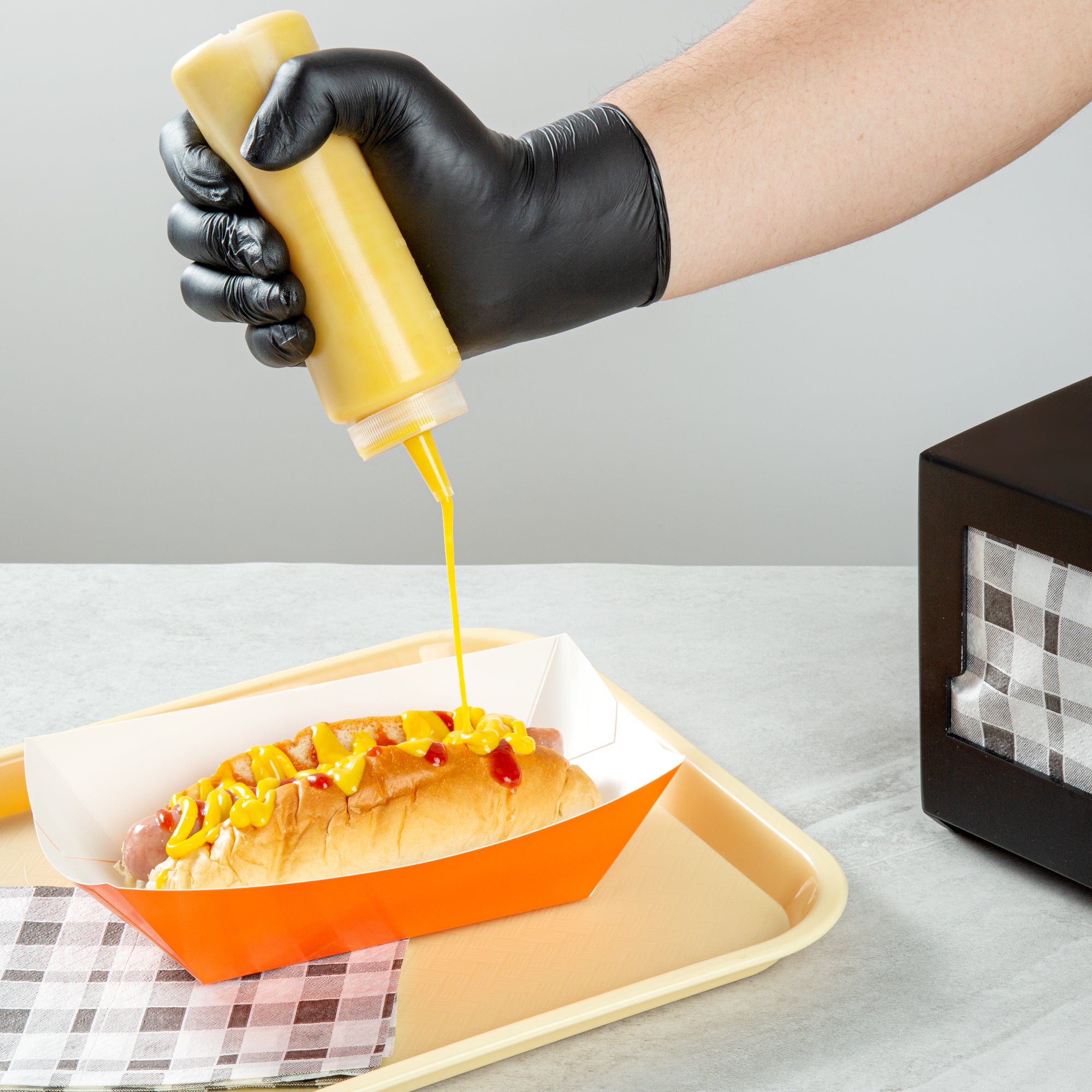 A precision bottle dispensing a condiment onto a hot dog